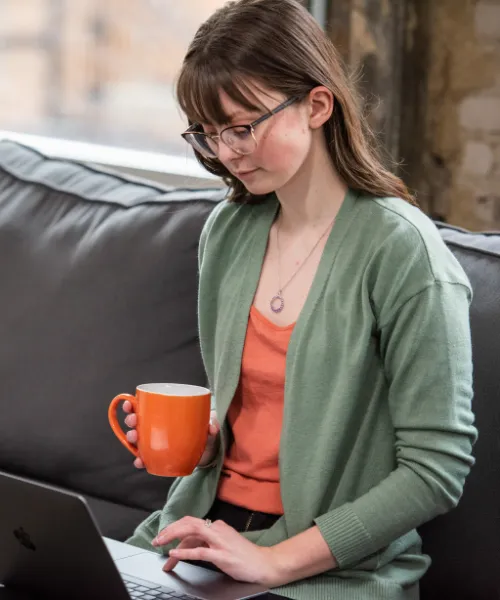 Madelyn Holifield of Click Control Marketing working on a laptop with orange coffee mug in hand.